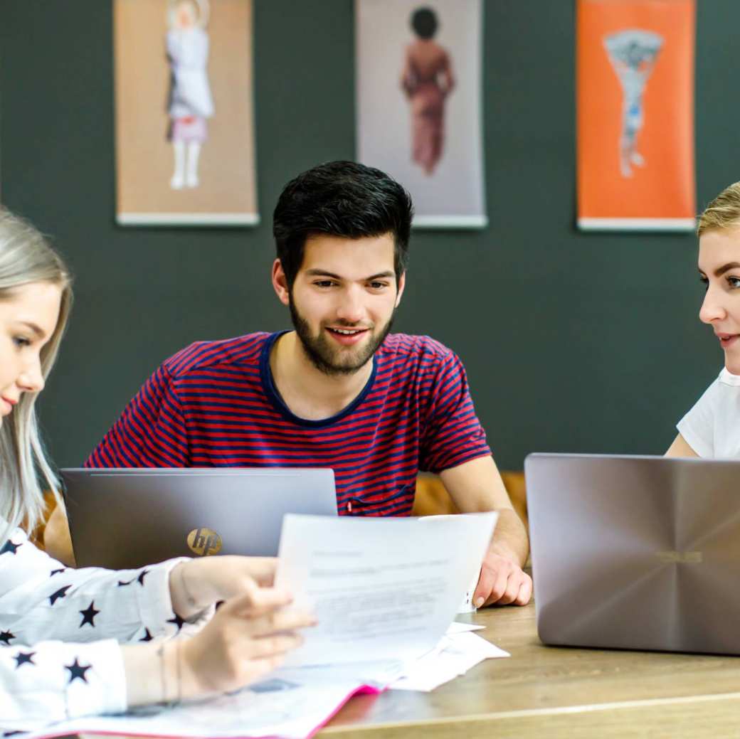 Twee studenten kijken naar wat hun medestudent aanwijst op het A4'tje. 