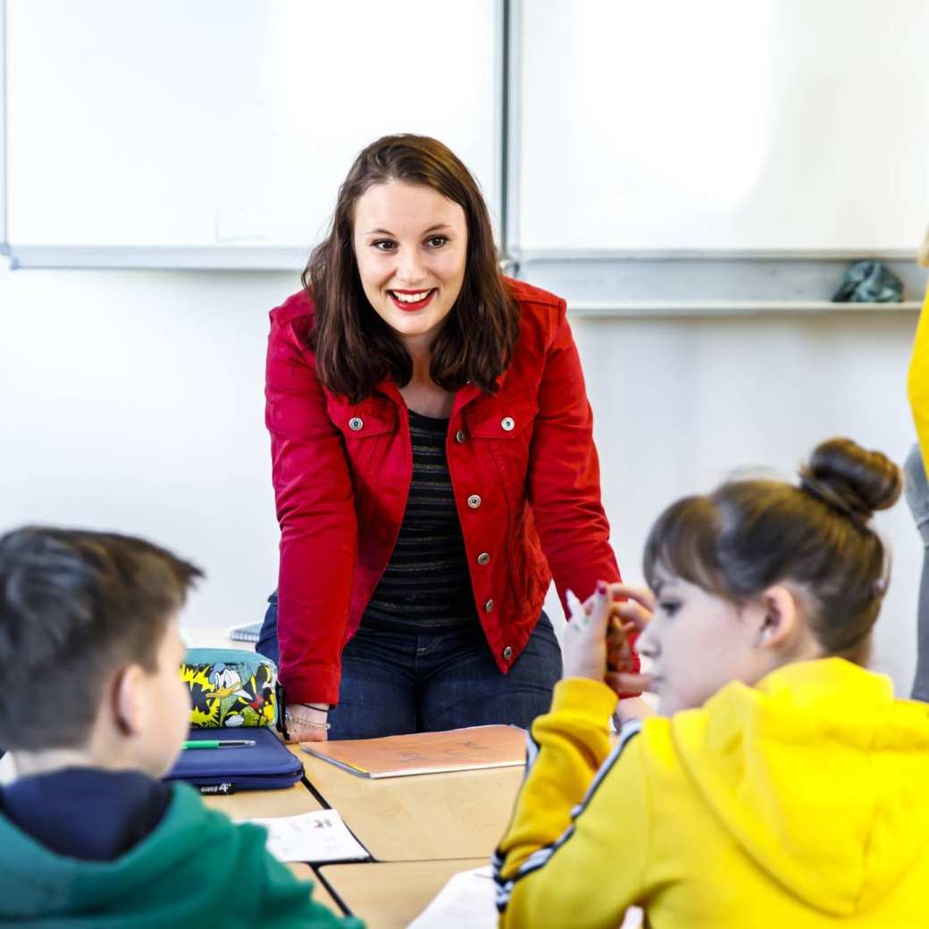 Docent luistert naar haar drie studenten die aan de tafel zitten te overleggen.