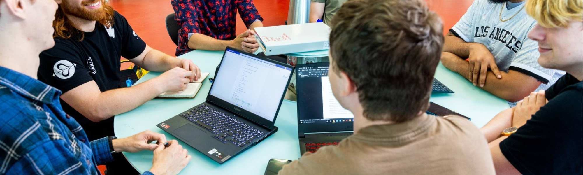 a group of engineering students -mechanical werktuigbouwkunde - working on a project together at a round table with laptops 