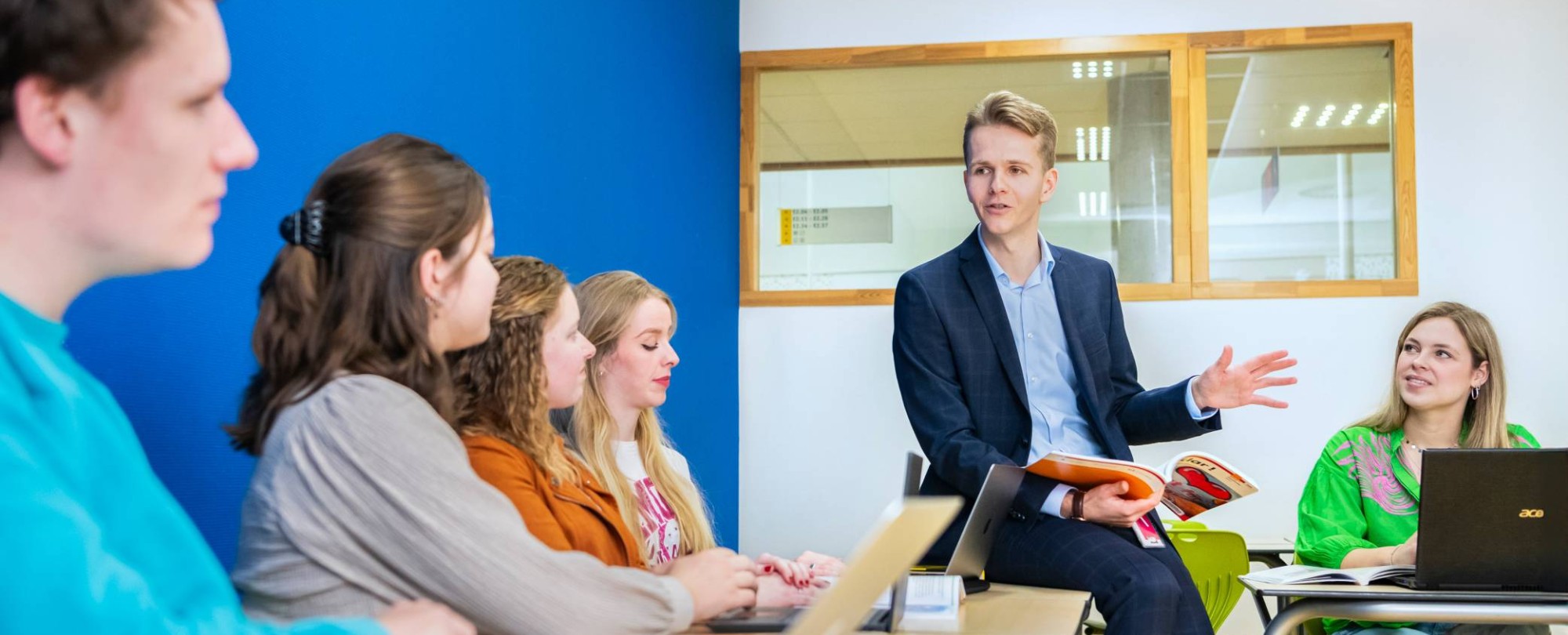 Duits docent bladert door studieboek en praat richting leerlingen