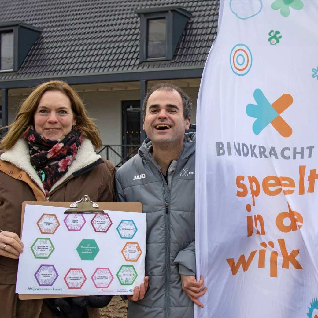 3 lachende mensen, een vrouw met rood haar, een man met kalend hoofd en grijze pufferjas en een vrouw met Bindkracht10 jas zijn de wijk ingegaan met de wijkwaardenkaart die ze in hun hand houden.