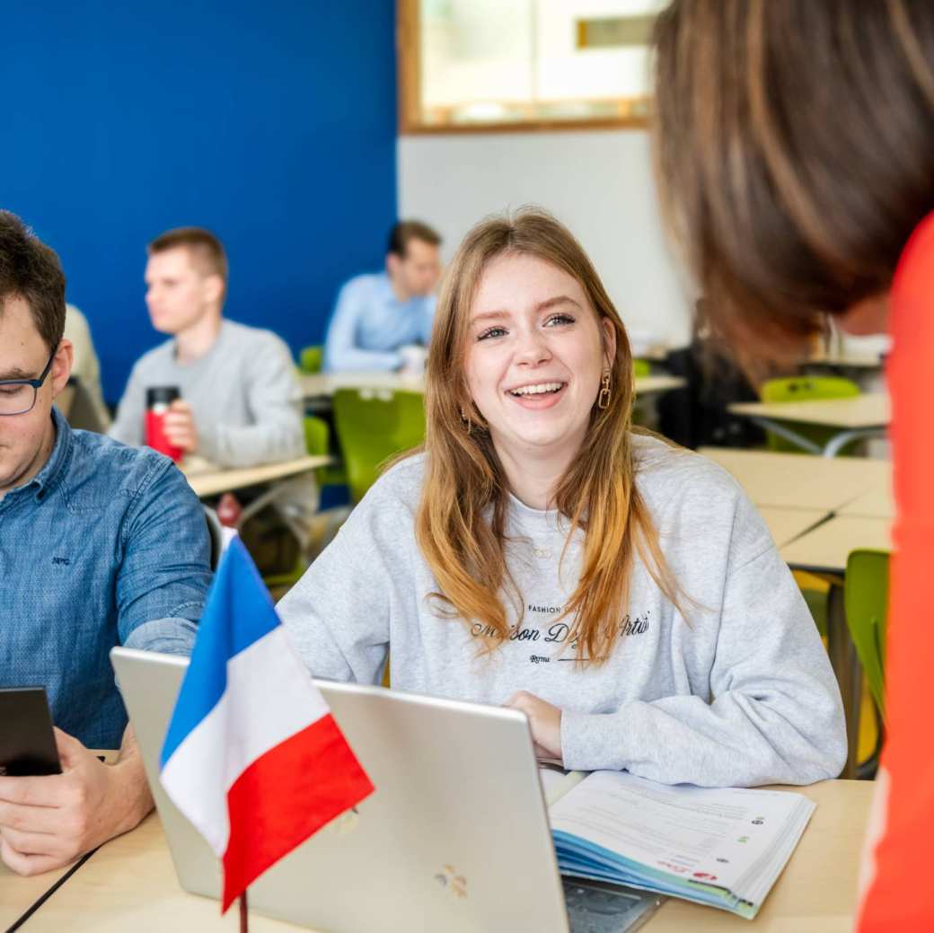 Twee studenten kijken naar hun docent die de bladzijde uit het boek omslaat.