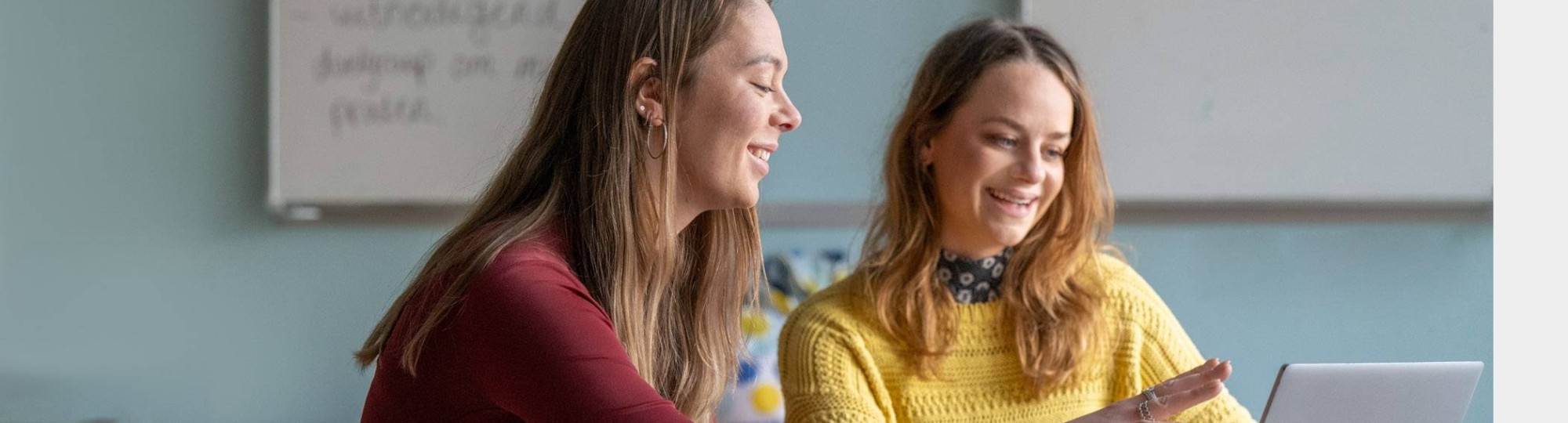 Twee studenten kijken lachend naar hun laptop.