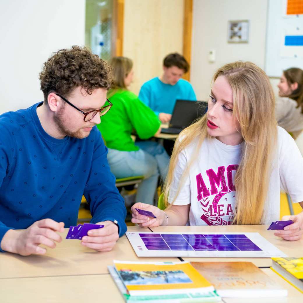 Twee studenten werken samen achter de laptop in het I/O gebouw en kijken lachend naar het scherm.