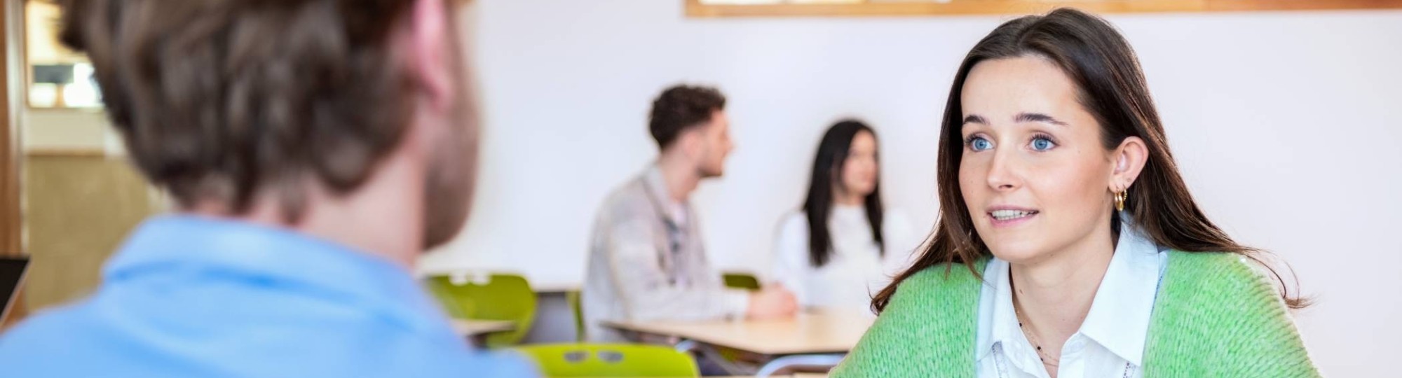 Twee studenten kijken lachend naar hun docent die tegenover hen zit.