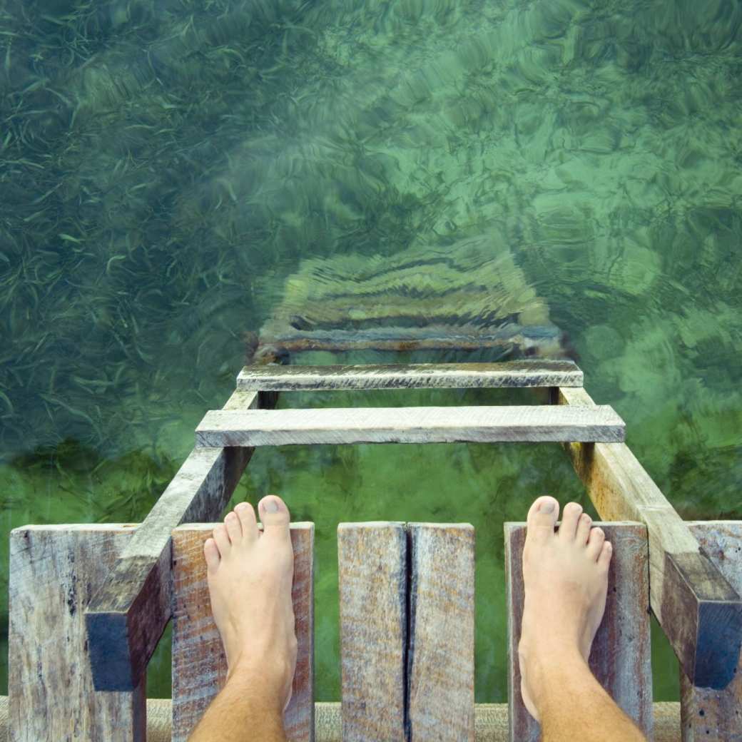 stockfoto van voeten op een vlonder aan de rand van groen water