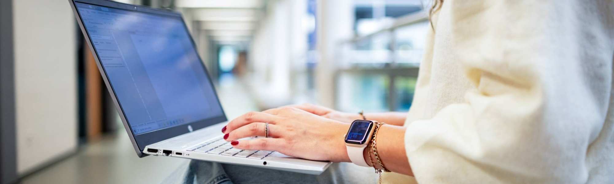 Student van de bachelor Commerciële Economie deeltijd, duaal in gang met laptop.