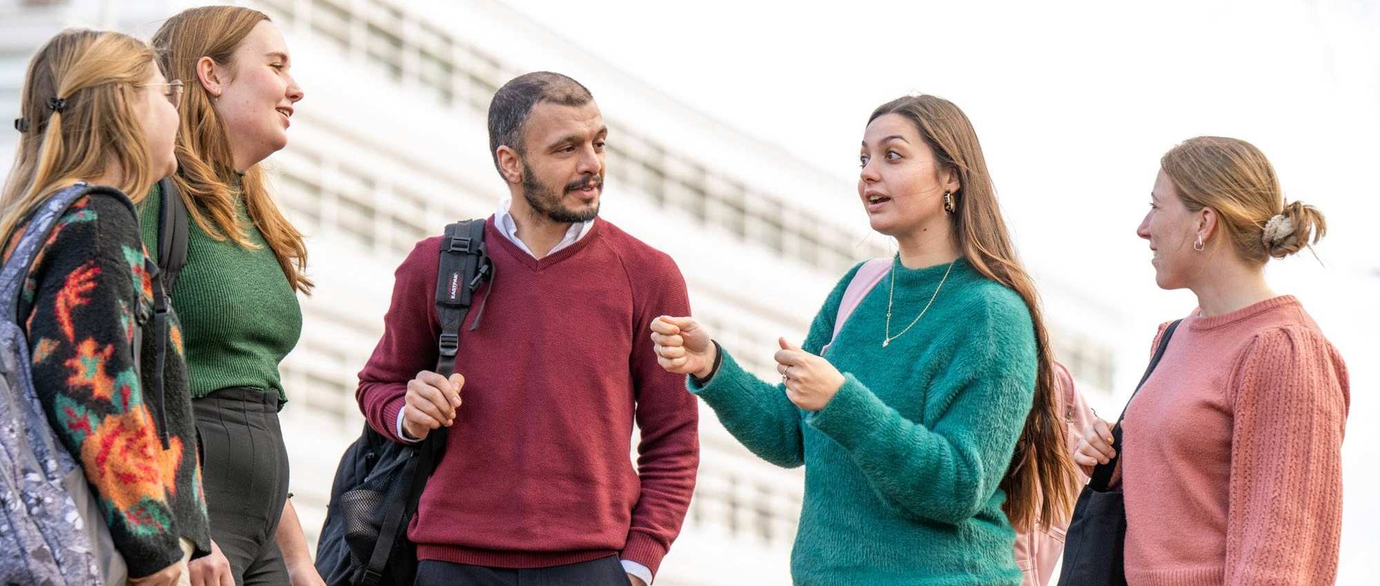 5 studenten praten buiten met elkaar. 