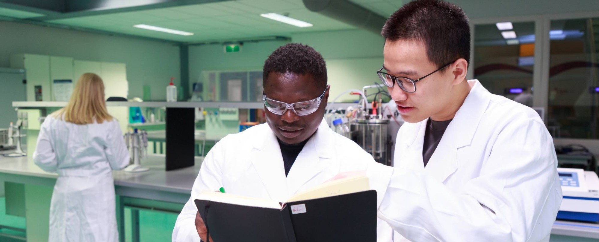 Studenten master Life Sciences Alain Barhasima en Dat Le werken in een biologielab. Op de rug Lisan Scholten