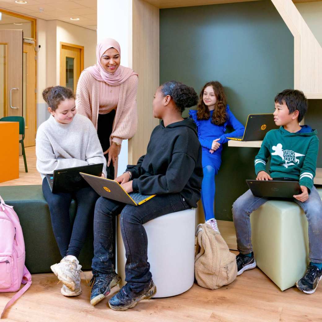 Leerlingen zitten bij elkaar in de hal van de school, docent staat erbij