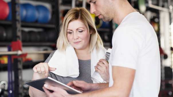 fitnesstrainer in de sportschool in gesprek met een blonde vrouw met overgewicht