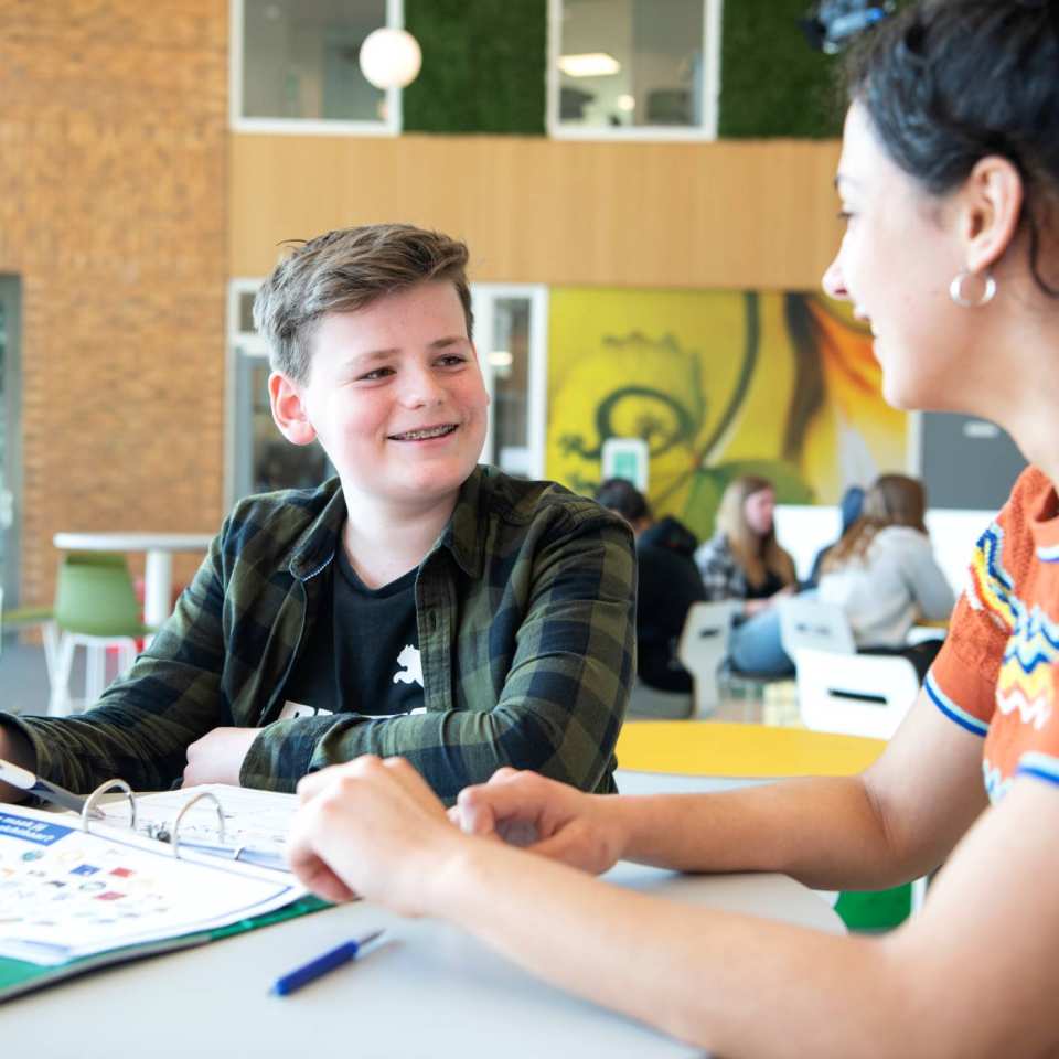 jongen werkt aan tafel en docent helpt