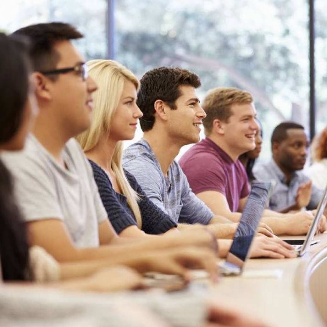 Klas studenten aan ronde tafel achter hun laptop.