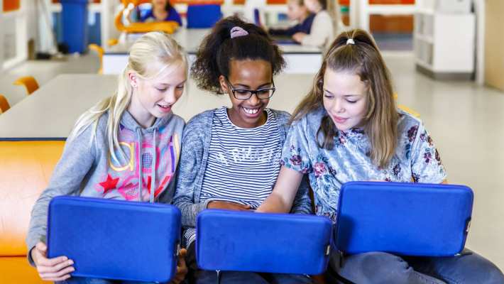 Drie kinderen zitten op een rijtje achter hun laptop met blauwe hoes.