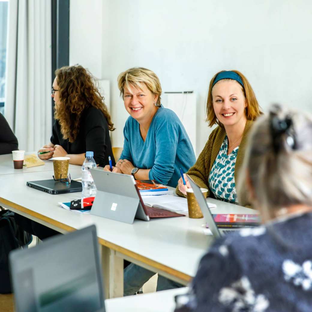 Een hoek van een klaslokaal met 6 dames die met elkaar overleggen.