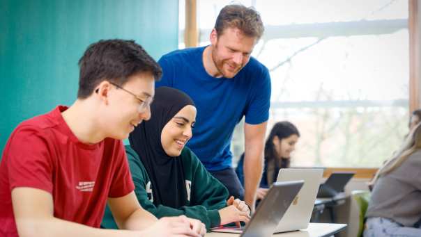 Docent kijkt mee met studenten op de laptop