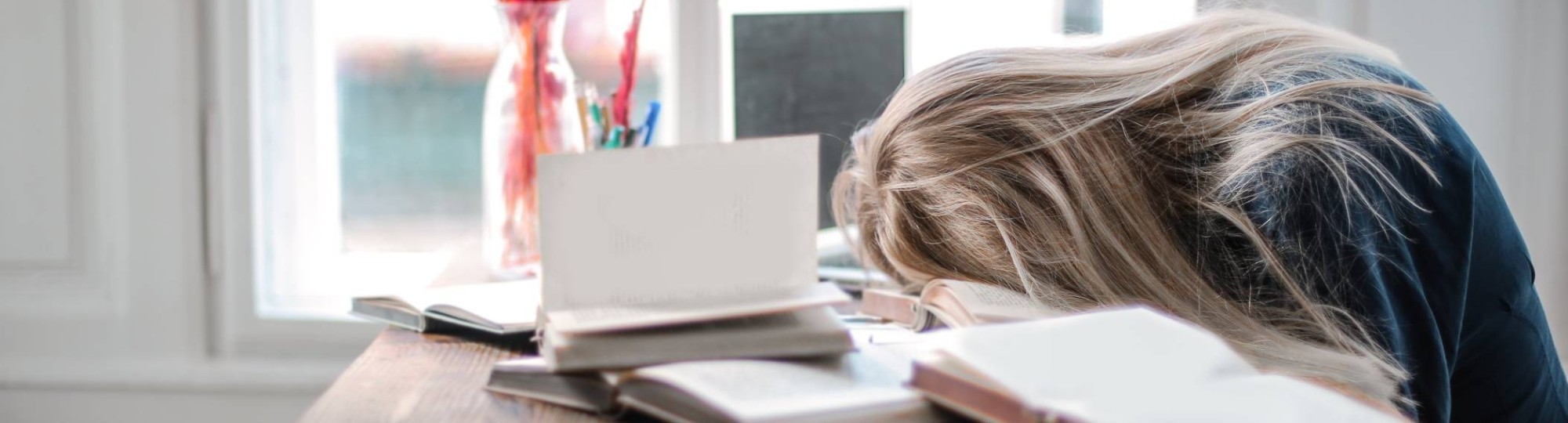 Leerling ligt op tafel tussen de boeken omdat ze moe is tijdens het studeren.