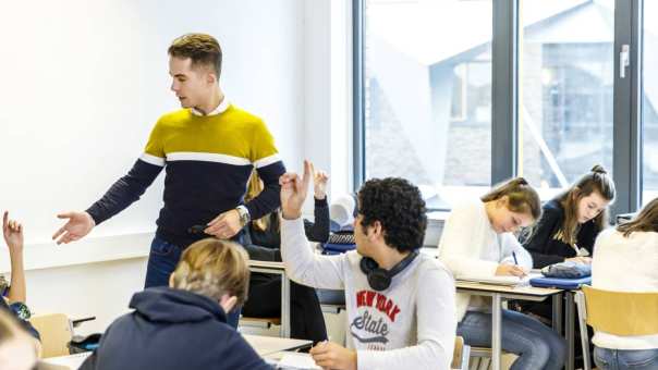 Docent op het Citadel College loopt door het klaslokaal om vragen van de leerlingen te beantwoorden die de vinger in de lucht hebben.