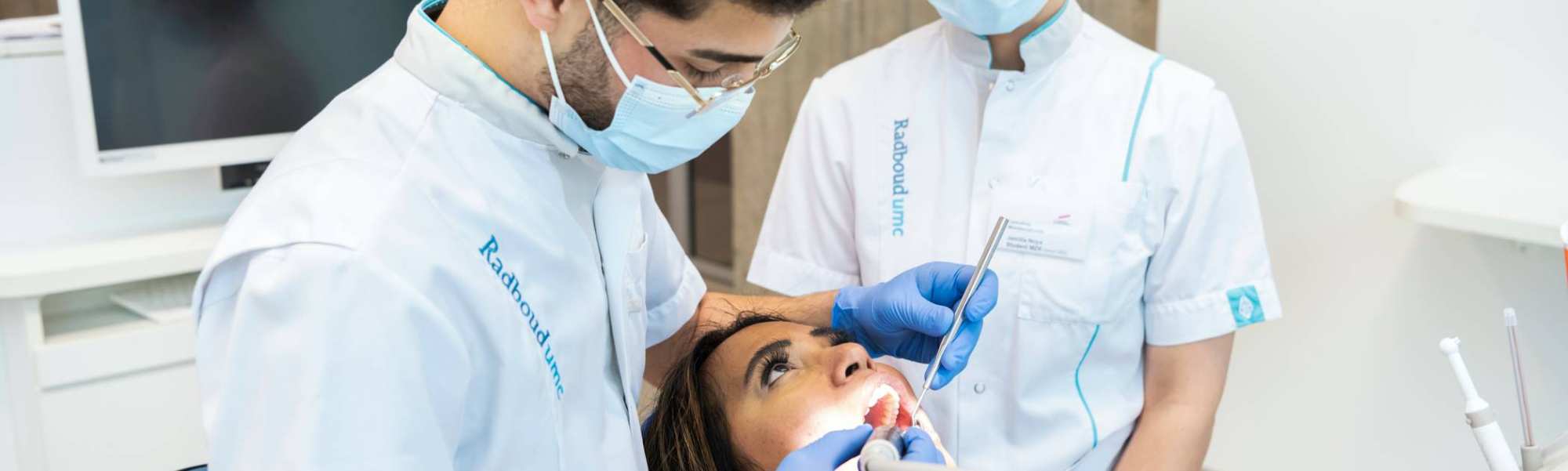 2 studenten kijken in de mond van een patient. 1 heeft materialen vast, de ander kijkt toe.