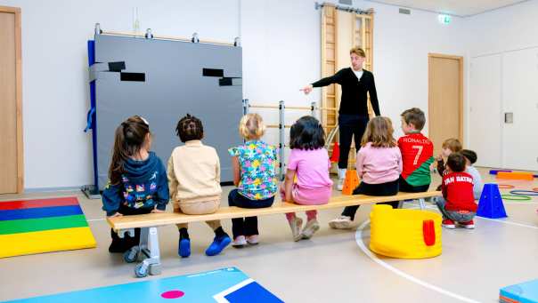 De kleuters op de school De Ommelander. De leraar wijst de kleuters iets aan in de gymzaal. 