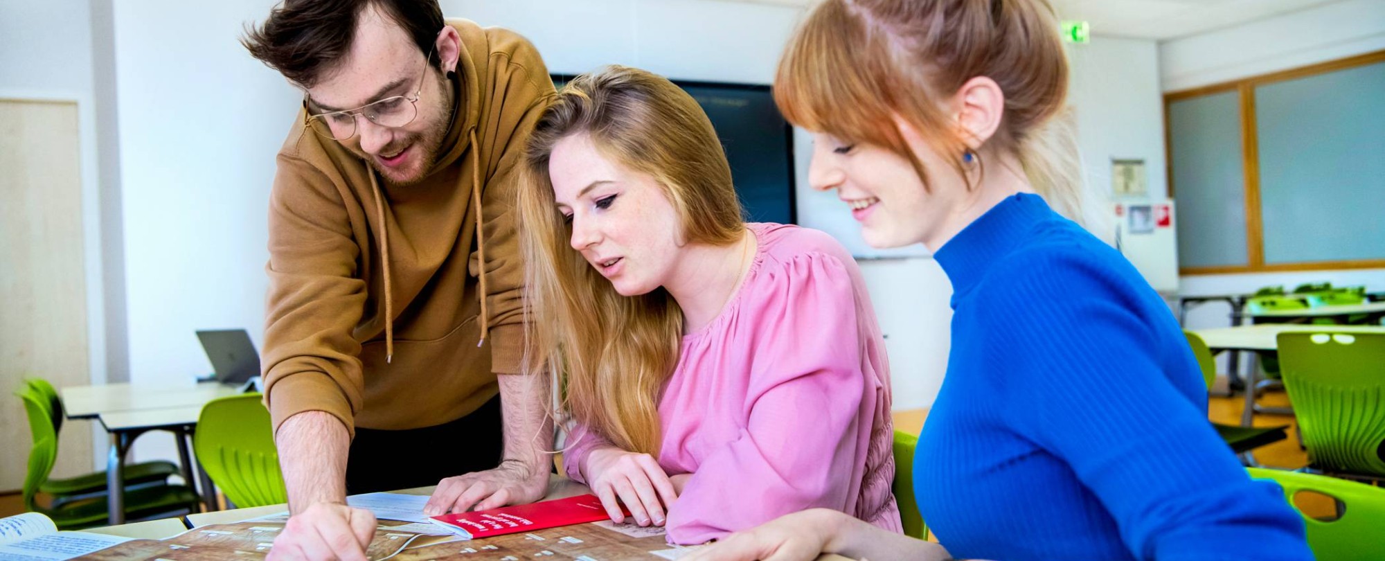 Drie studenten kijken aandachtig naar de kaart die voor hen ligt en ontrafelen wat erop staat.