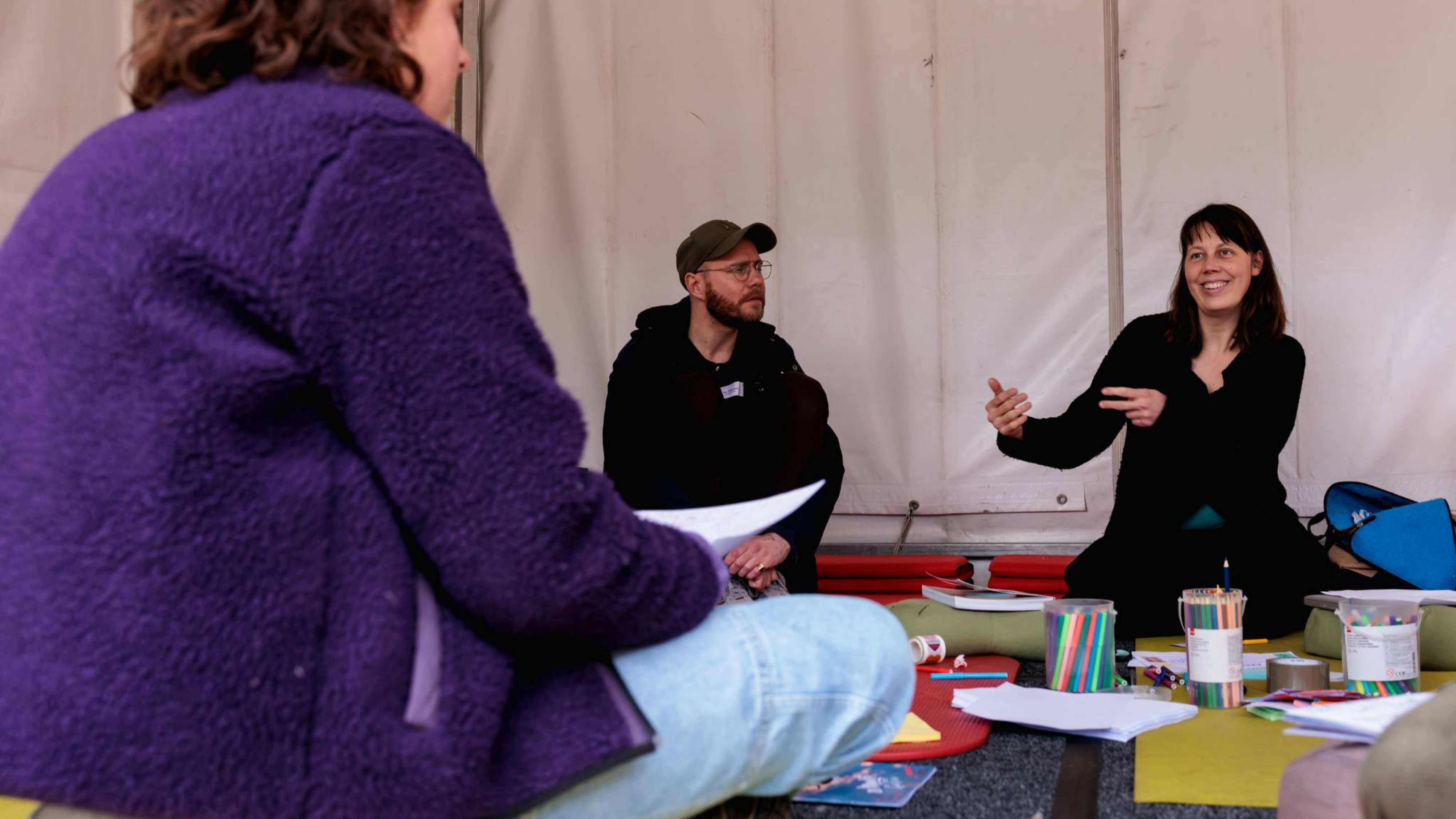 Workshopgever geeft gebarend uitleg aan deelnemers in witte tent