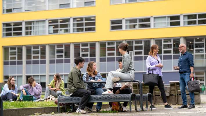 Studenten zijn buiten, zitten aan picknicktafel en in het gras. Buiten op campusterrein Arnhem. 