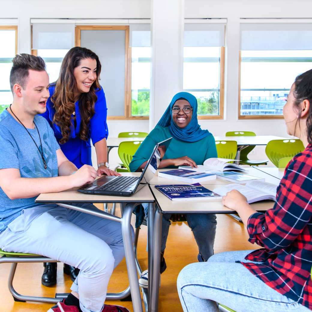 Docent kijkt via de laptop mee naar het werk van haar drie studenten. 