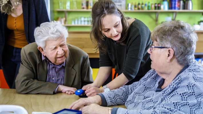 bijeenkomst wijkatelier lindenholt- ouderen aan tafel studente staand in het midden