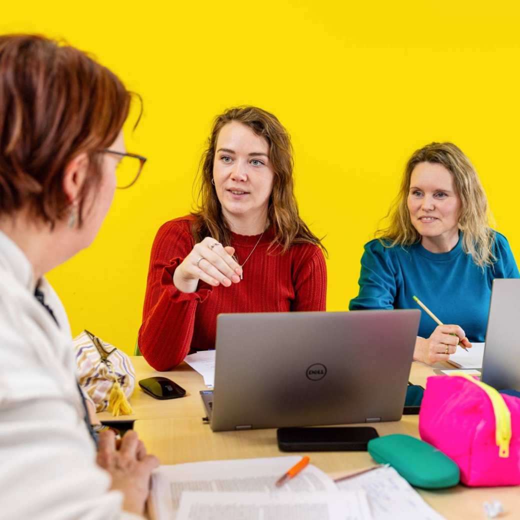 Een student wijst lachend iets aan in de atlas en de andere student kijkt nieuwsgierig toe.