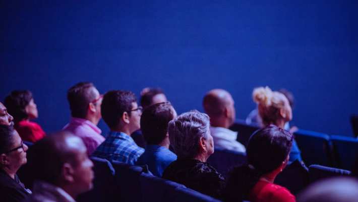 Een beeld van mensen die in een zaal zitten te luisteren