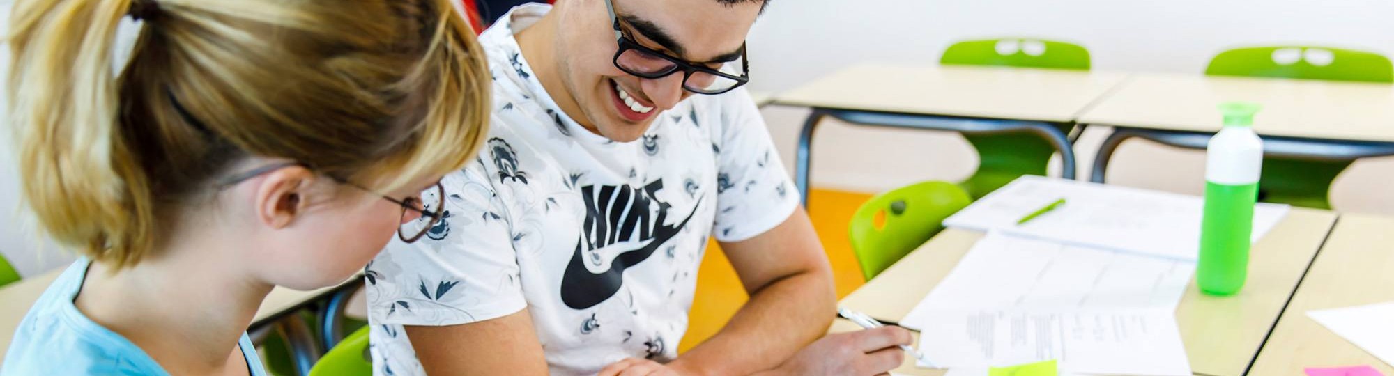 Twee studenten lezen de opdrachten op de werkbladen, die voor hun op de tafel liggen. 