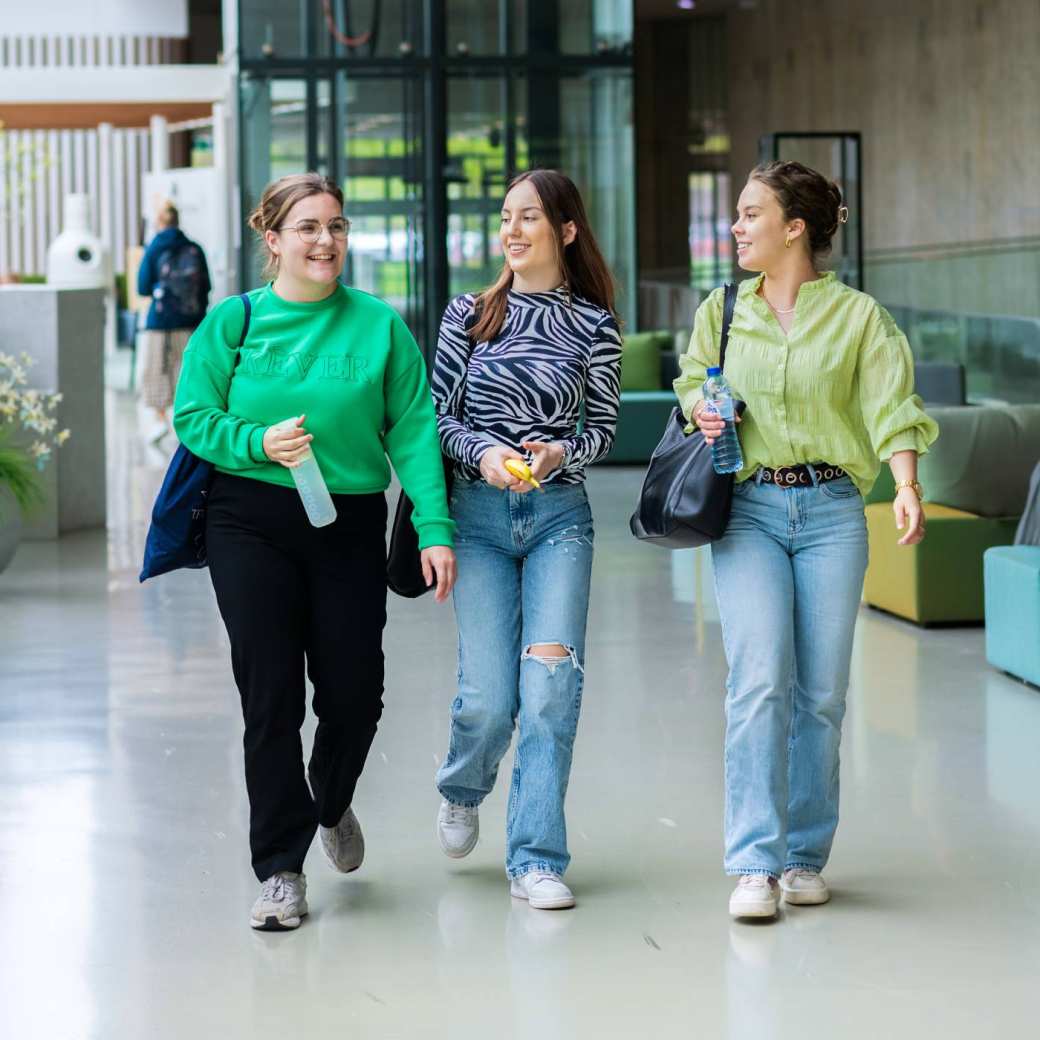 3 studenten lachen en lopen door de lege gang.