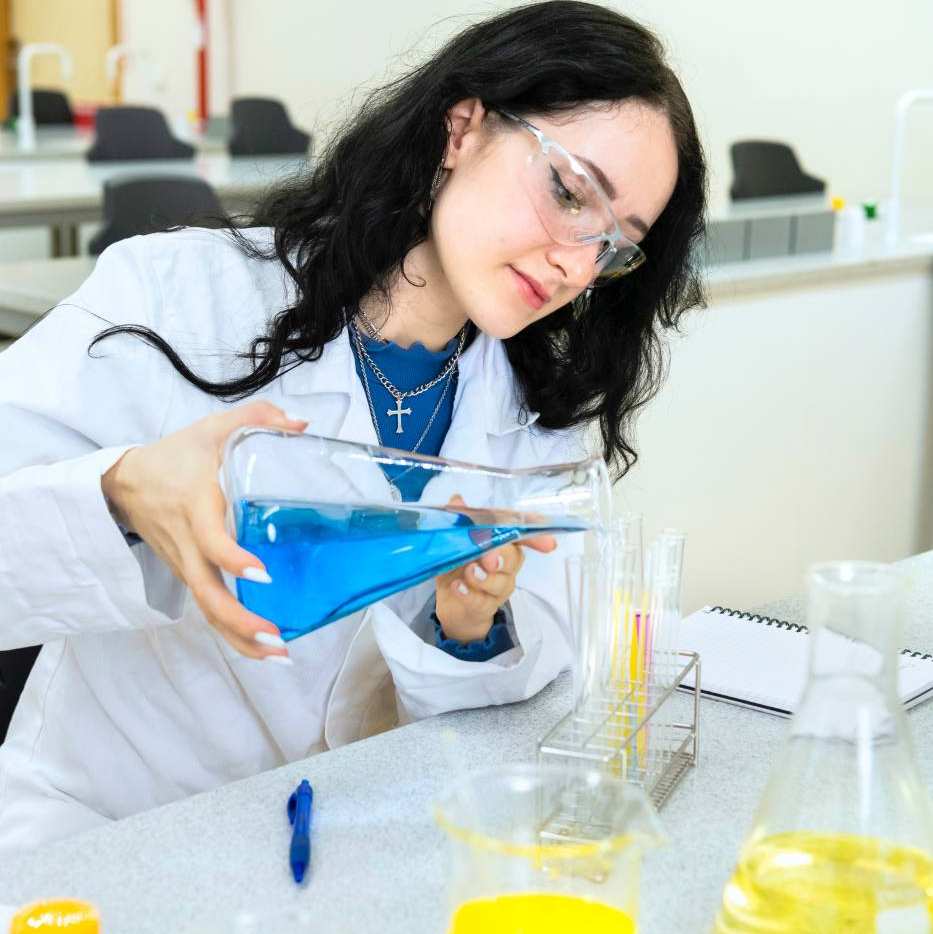 Een student schenkt blauwe vloeistof in buisjes.
