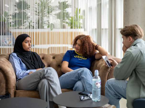 Studenten zitten samen op een bank, te chillen/relaxen. In gebouw K35. 