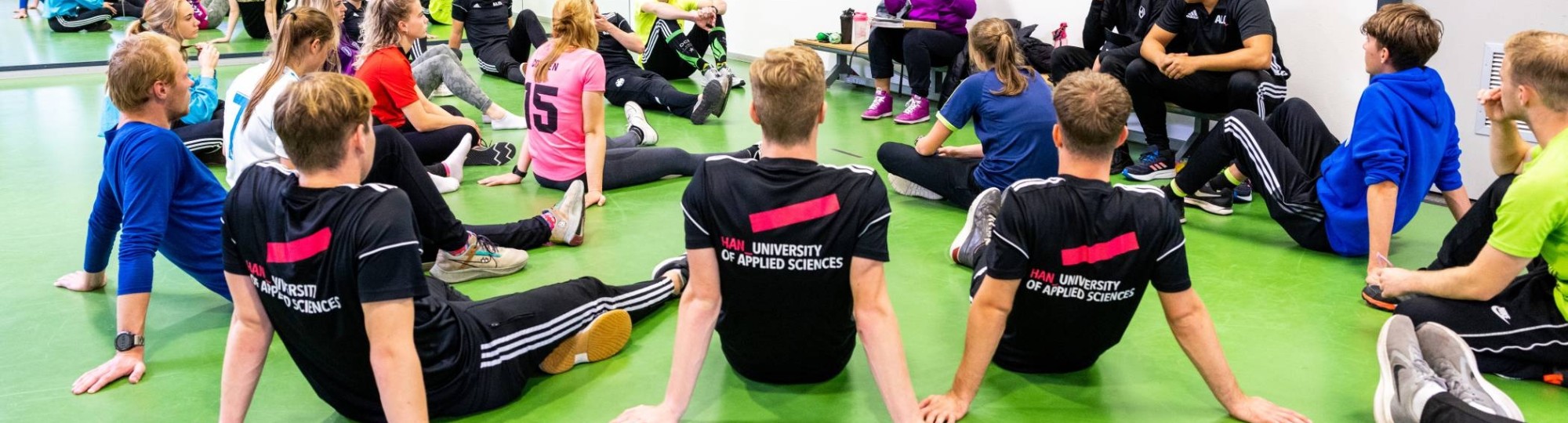 Studenten luisteren in de sportles naar docente.