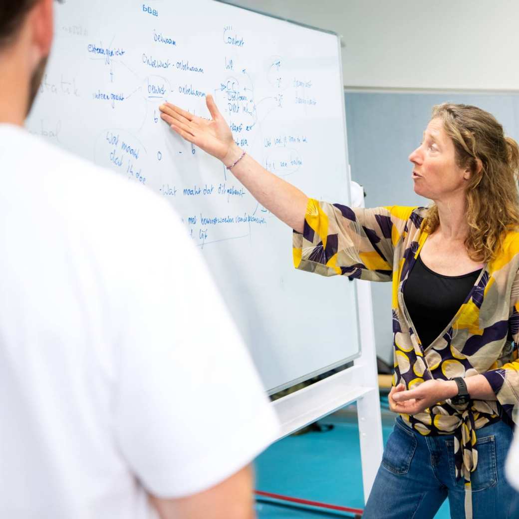 Docent geeft uitleg bij bord aan 2 studenten tijdens les PMT deeltijd