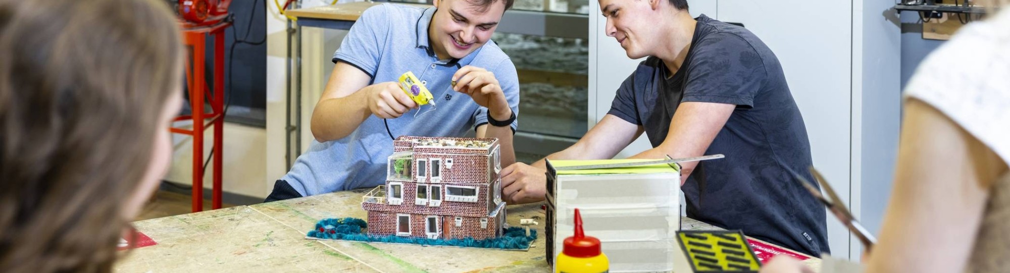 vier studenten zetten in de werkplaats van HAN Bouwkunde hun houten maquettes met houtlijm in elkaar