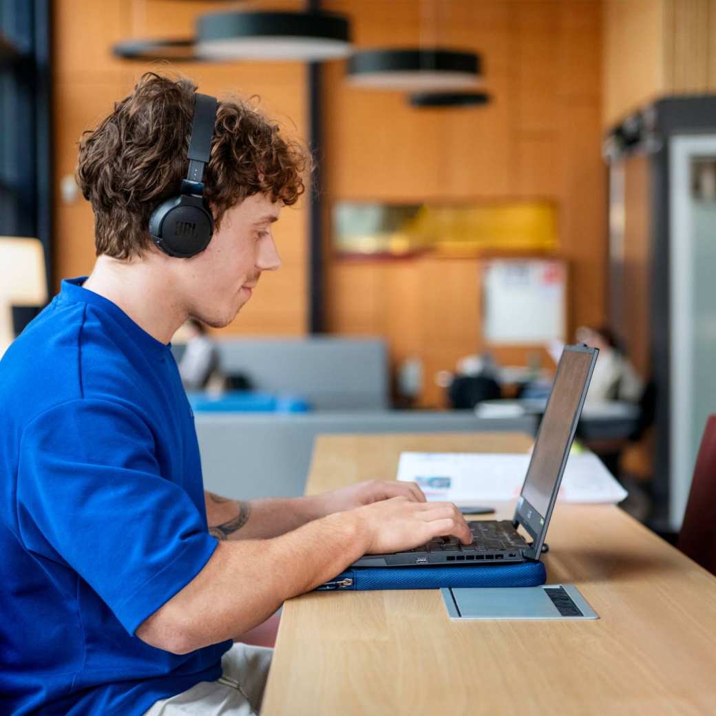 Student ICT werkt met koptelefoon aan een laptop.