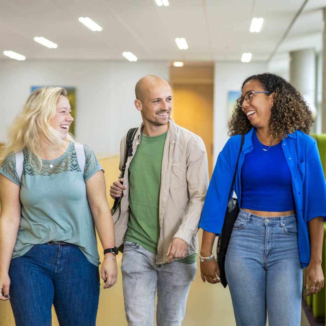 Drie studenten Leraar Wiskunde lopen lachend naast elkaar op de gang in de school