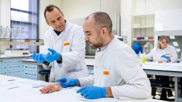 Een docent geeft uitleg over hechttechnieken aan een Physician Assistant in opleiding