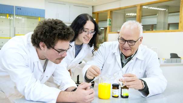 Twee studenten voeren met docent een proef uit in het lab