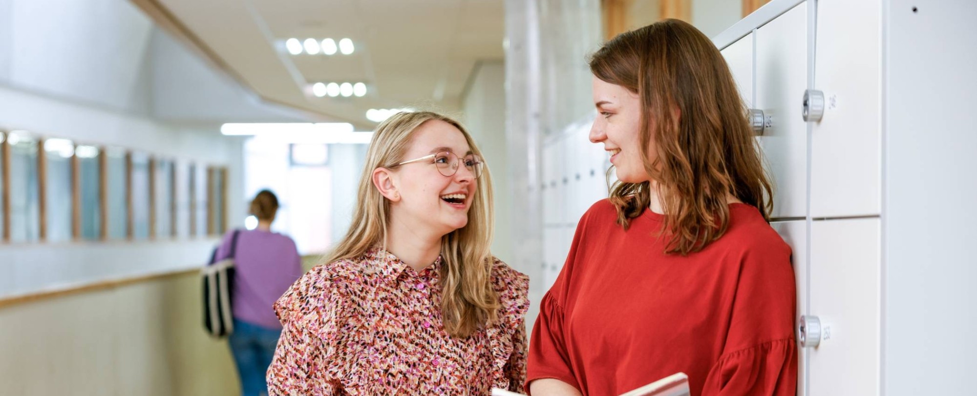 Twee studenten kijken elkaar lachend aan op de gang van het I/O-gebouw.