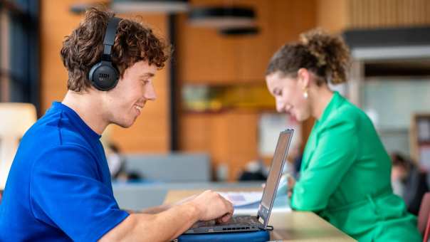 2 studenten zijn zelfstandig aan het werk, de voorste jongen draagt een koptelefoon.