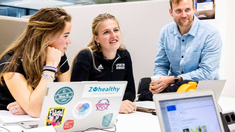 Studenten achter laptop lachen met docent Lennart.