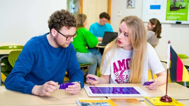 Twee studenten spelen een kaartspel met blauwe kaartjes in een gekleurd leraar Duits lokaal.
