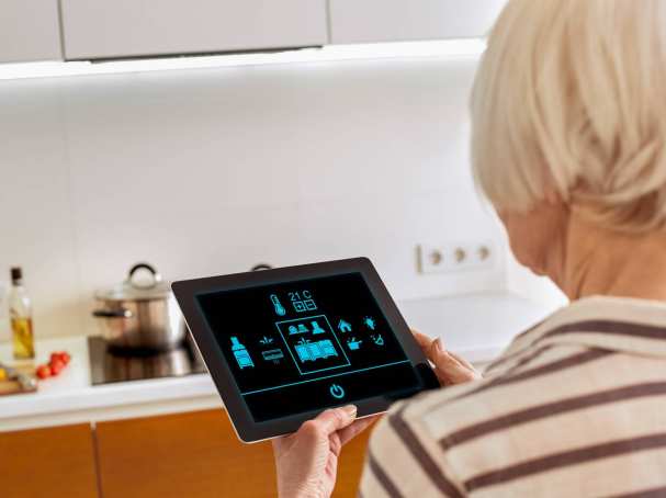 Oudere dame werkt met een tablet om op een innovatieve manier haar woning te bedienen.