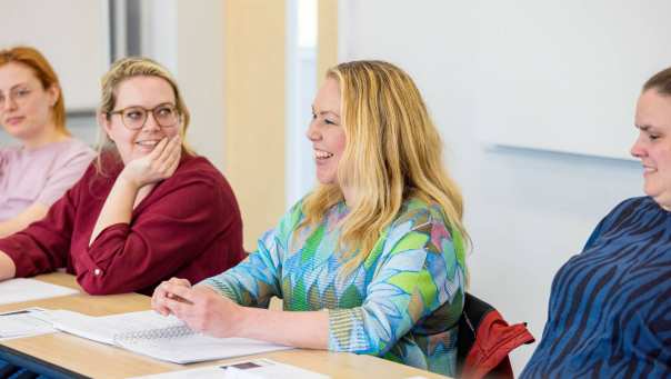 Vrouw is in gesprek en aan het lachen tijdens de cursus acute pijn service. Andere vrouw kijkt haar aan op de achtergrond.