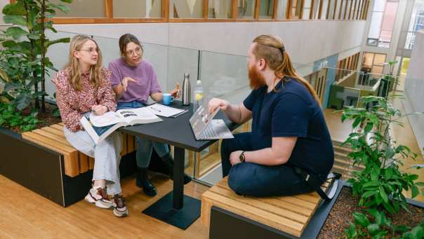 Drie studenten werken in I/O-gebouw en overleggen samen.