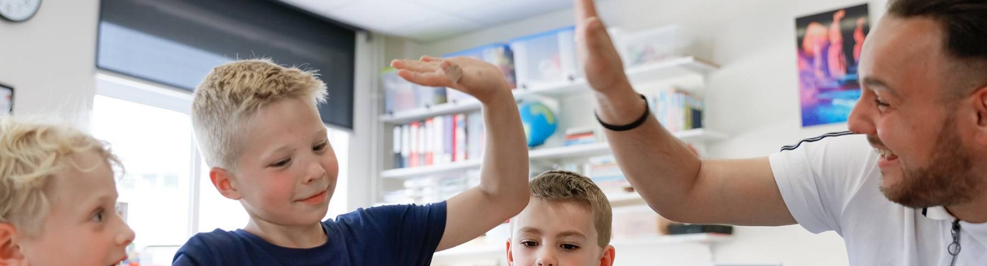 Leraar zit met drie kinderen achter de iPad en geeft Ã©Ã©n van die leerlingen een high-five. 